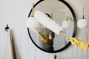 A person cleaning an elegant bathroom mirror with a fluffy duster and yellow gloves.